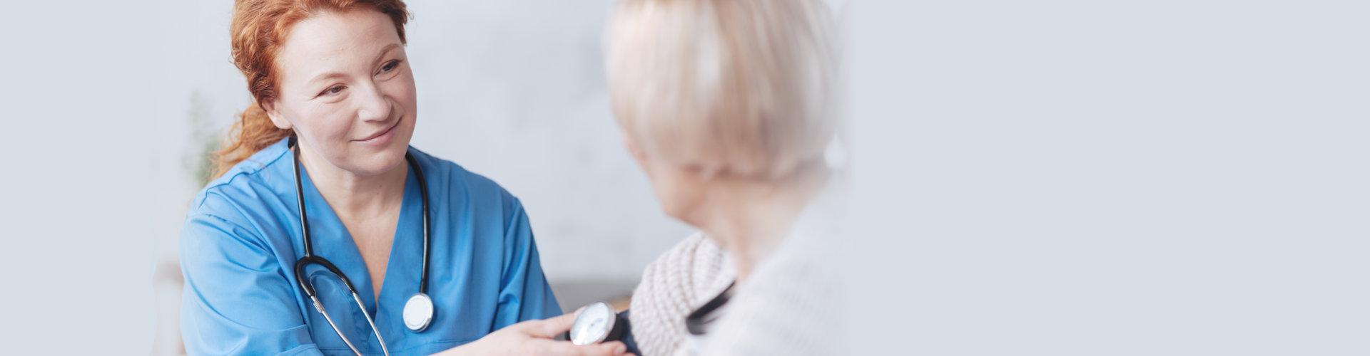 Selective focus on a tender nurse looking at her elderly patient with a slight smile on her face